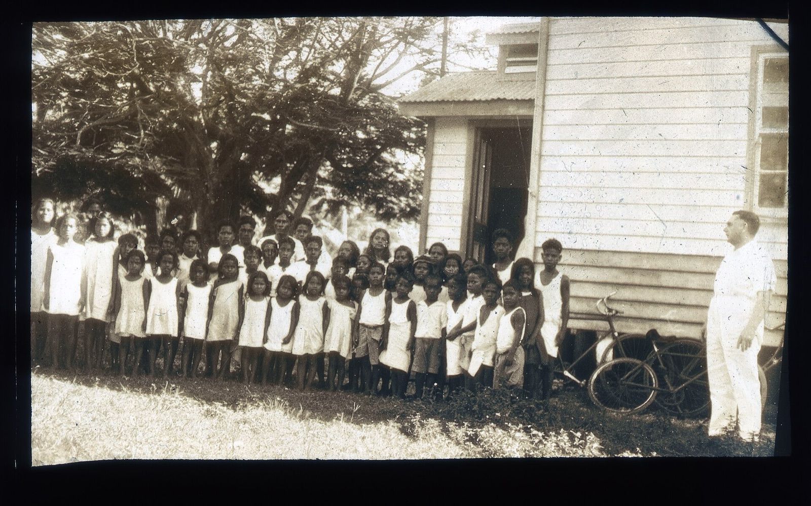 Nauruan schoolchildren lined up outside a wooden school building with their teacher